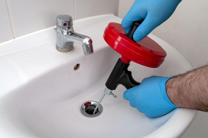 Person with gloved hands using an auger or drain snake to unclog a sink.